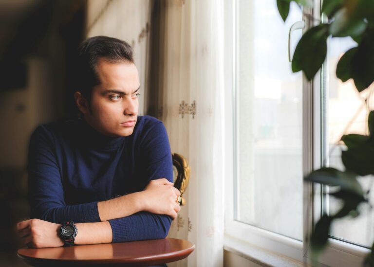 young man thinking deeply near window How to Build a Growth Mindset about personal growth