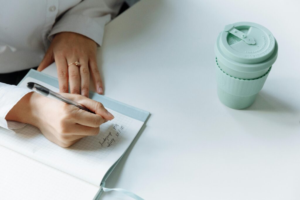 person writing daily rules in journal with coffee cup morning routine habits