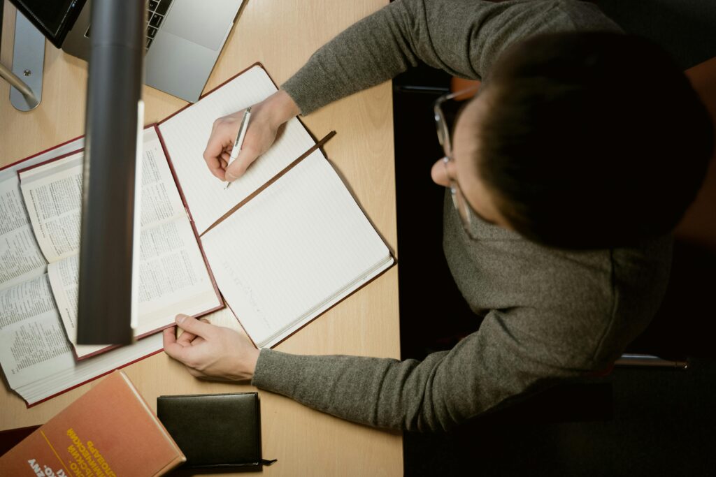 person writing daily habits and rules in notebook surrounded by books